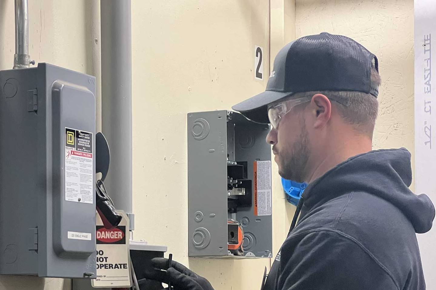 Person wearing safety glasses and gloves working on an electrical panel during hands-on electrical training