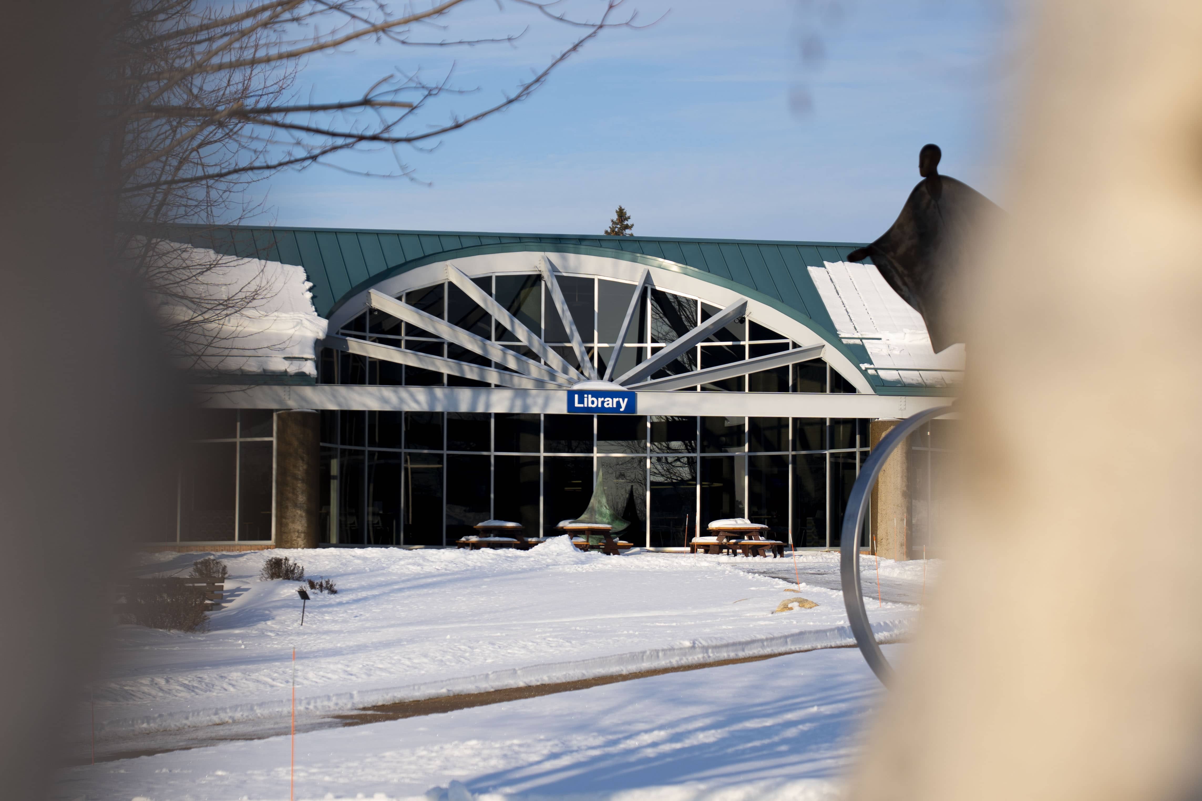 Exterior view of the North Central Michigan College Library in Petoskey, Michigan, with snow covering the ground and picnic tables outside