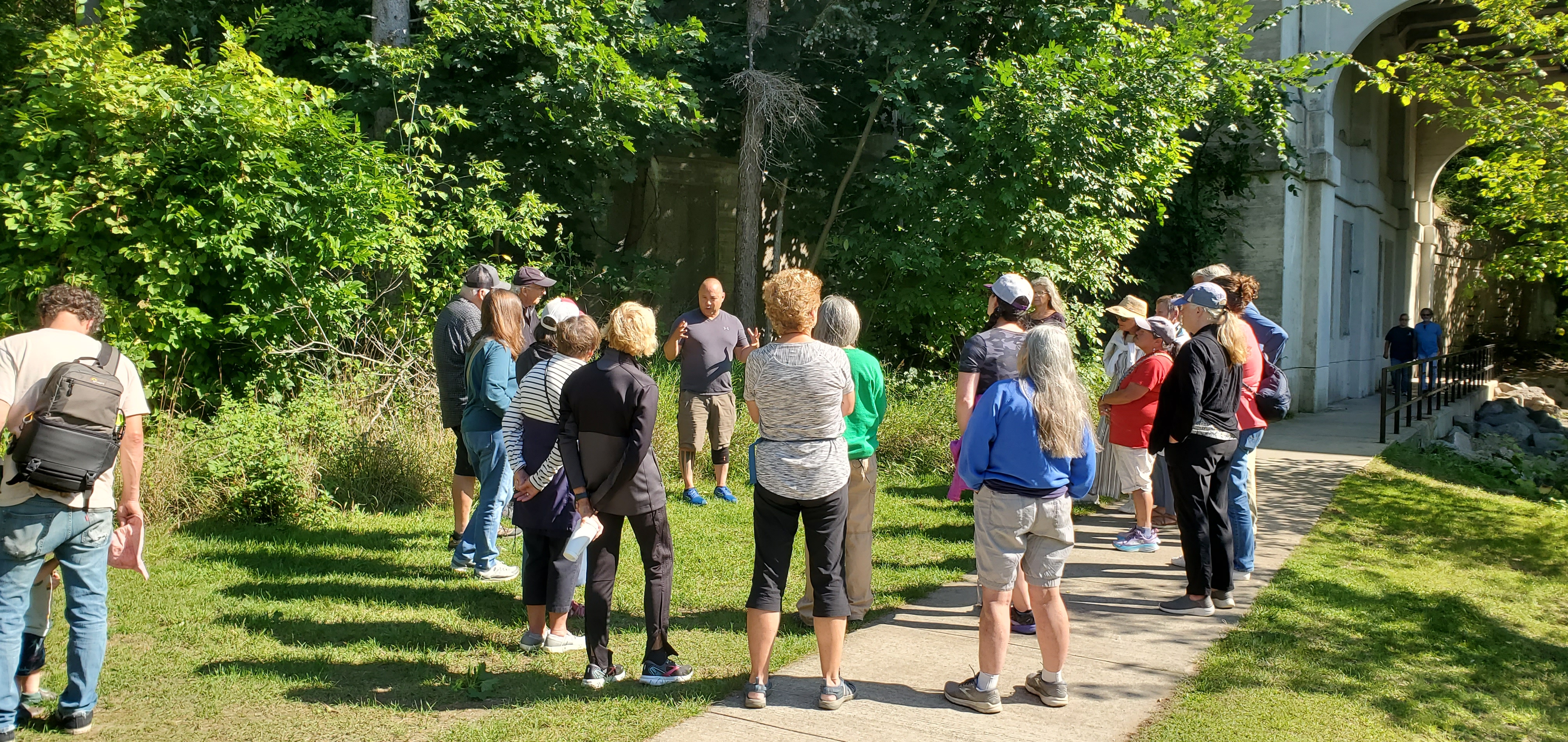 Participants gather outdoors for a guided educational tour, listening to a presenter discuss the surrounding natural environment