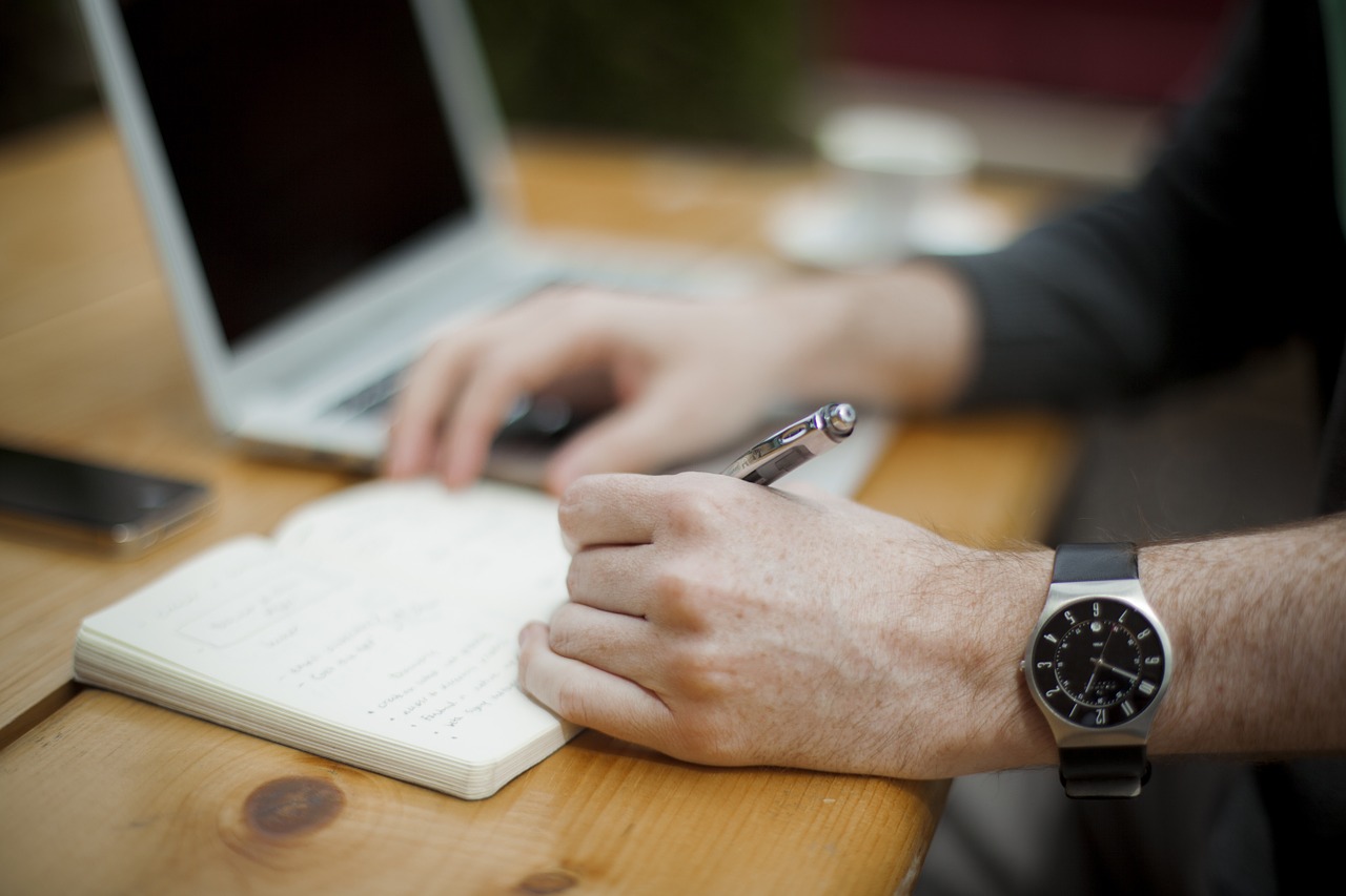 Man writing notes on a notebook and laptop