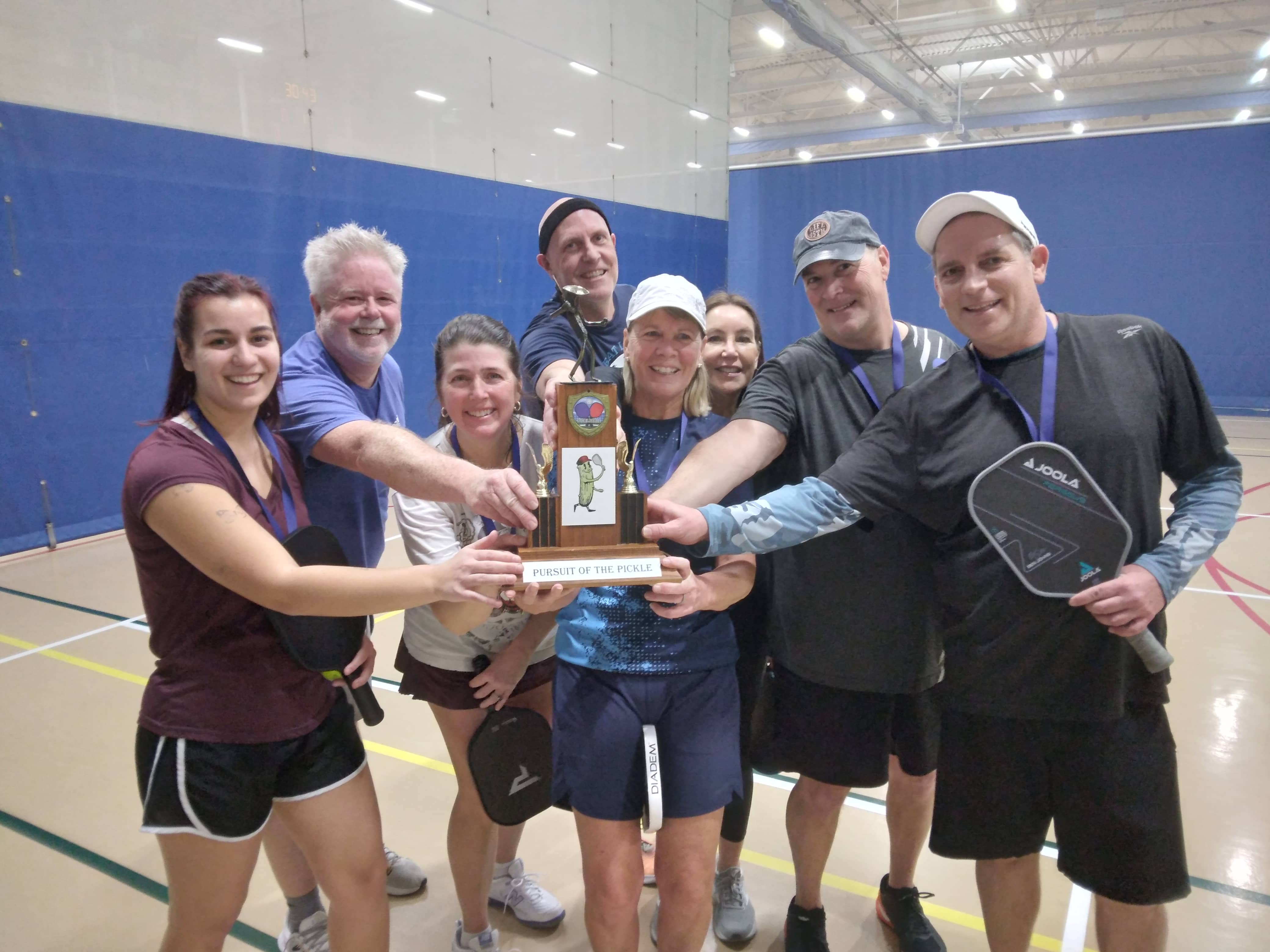 Eight pickleball players, standing with a trophy
