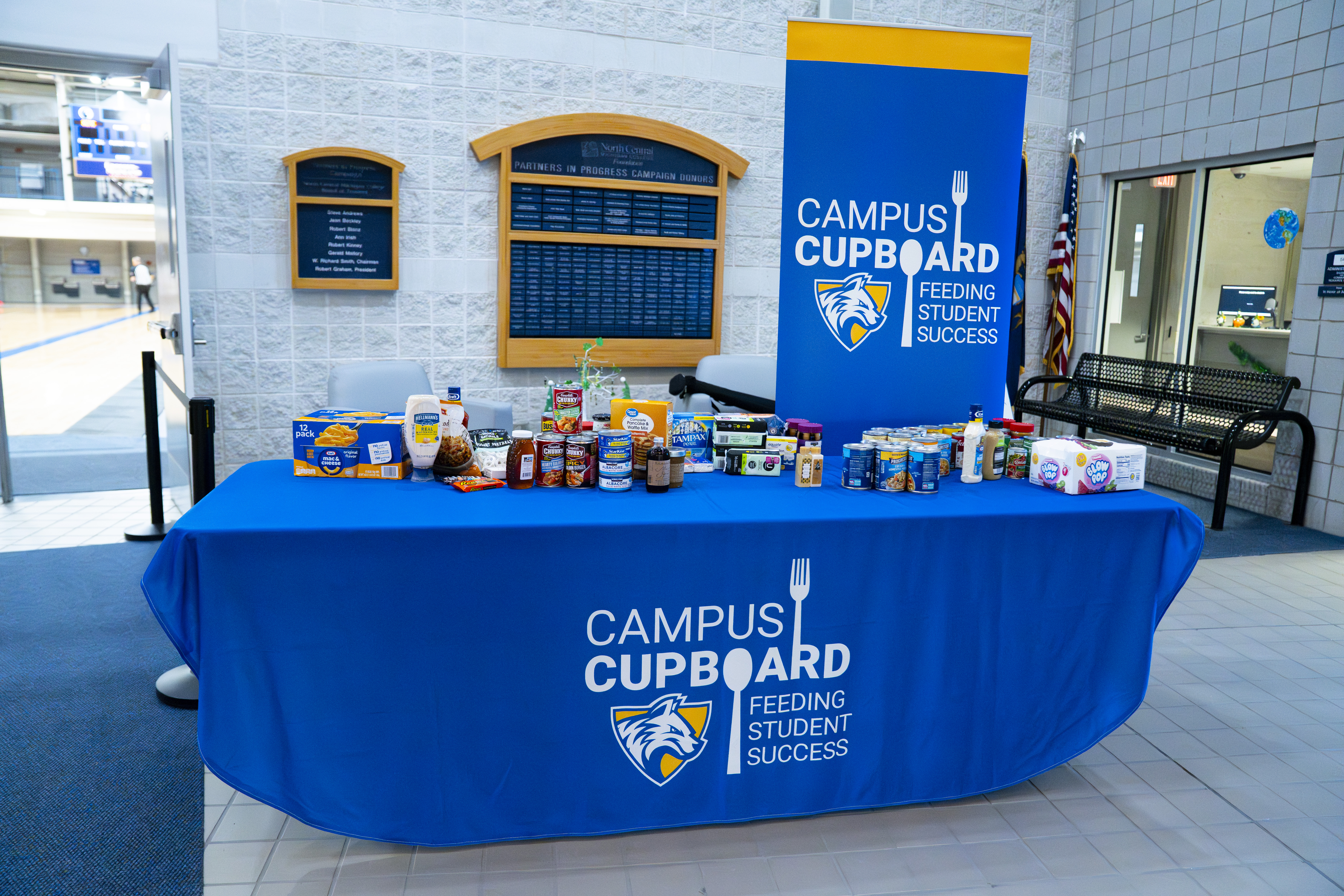 Campus Cupboard display table with nonperishable food and personal care items, with “Feeding Student Success” banner in background