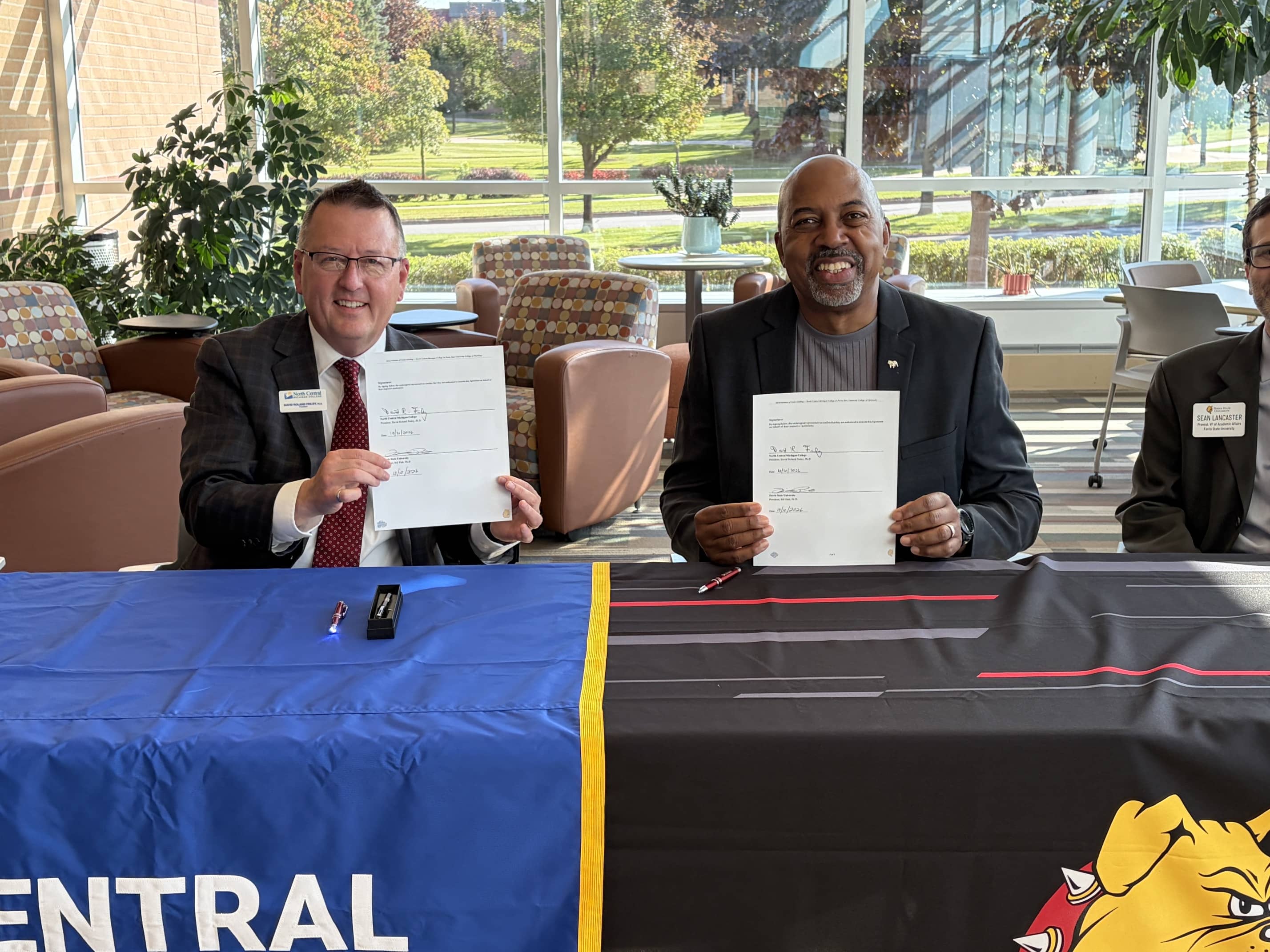 NCMC President David Roland Finley and Ferris State University President Bill Pink smile while holding signed agreements establishing transfer pathways in pharmacy and optometry.