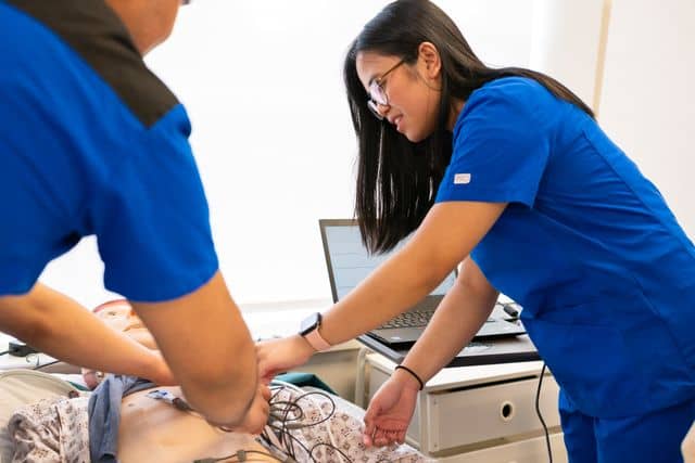 Students practice patient care skills on a simulation manikin in a nursing lab setting