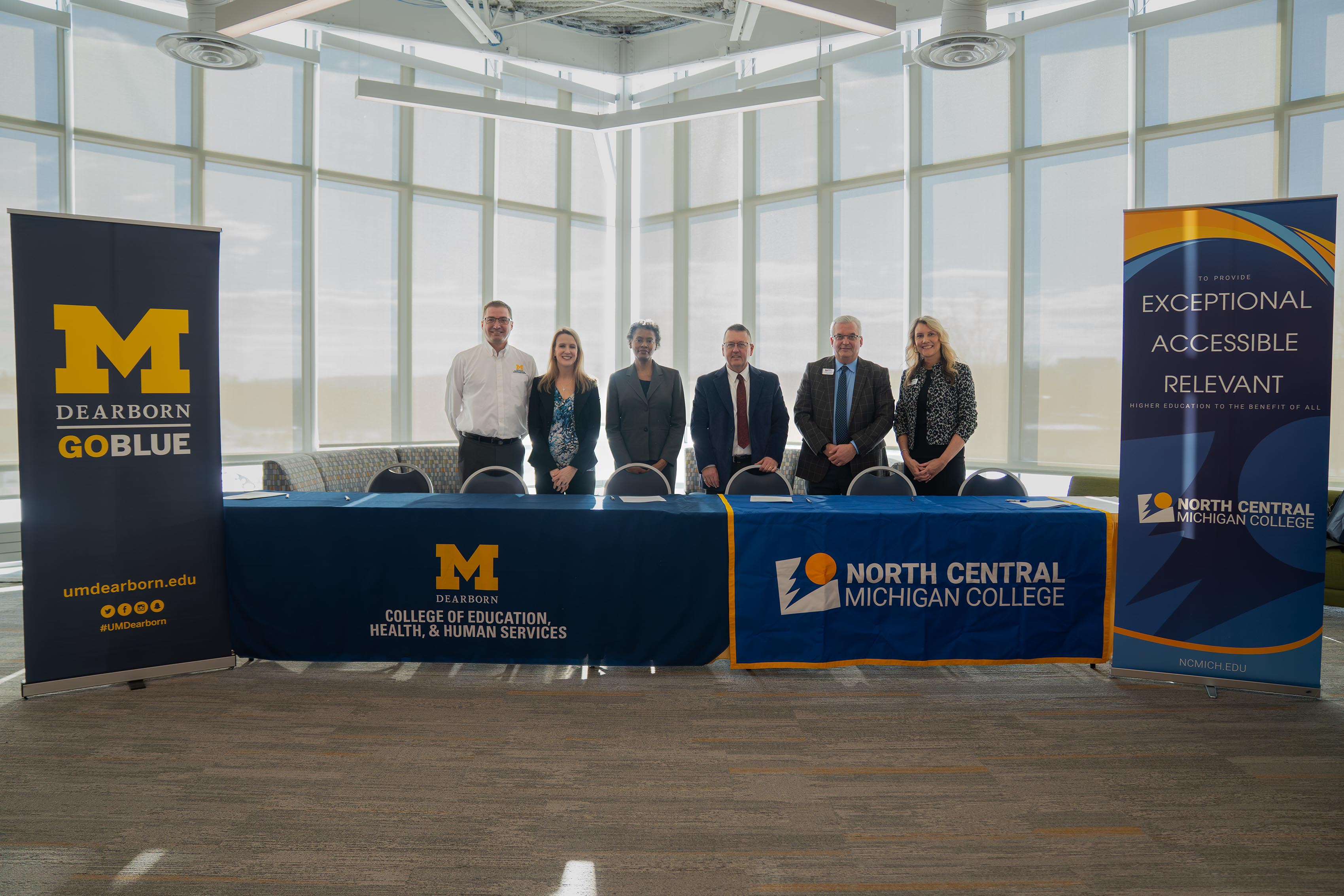 North Central Michigan College and University of Michigan–Dearborn leaders stand behind a signing table during a partnership event. From left, UM–Dearborn representatives Jonathan Larson, associate director of curriculum, transfer and enrollment initiatives; Danielle DeFauw, chair of the Department of Education; and Ann Lampkin-Williams, dean of the College of Education, Health & Human Services; followed by David Roland Finley, NCMC president; Stephen Strom, NCMC vice president for Academic and Student Affairs; and Michele Andrews, NCMC dean of business, education and adjunct faculty.