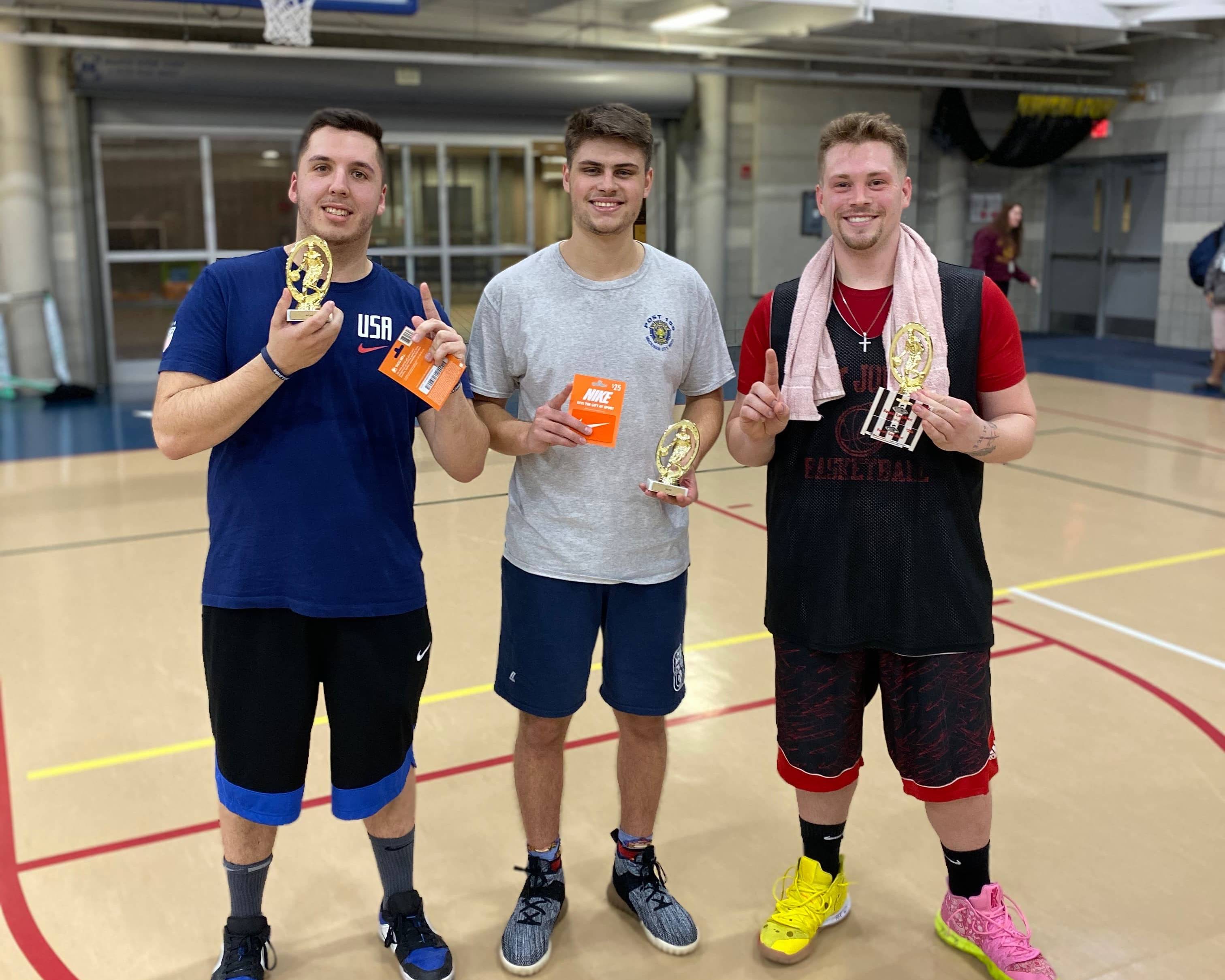 Three male basketball players holding trophies